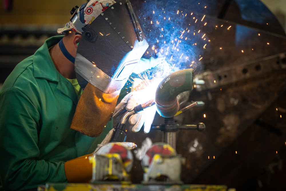 Welder fabricating stainless steel piping at Herman Goldner Co., Inc. for modular HVAC and mechanical systems.